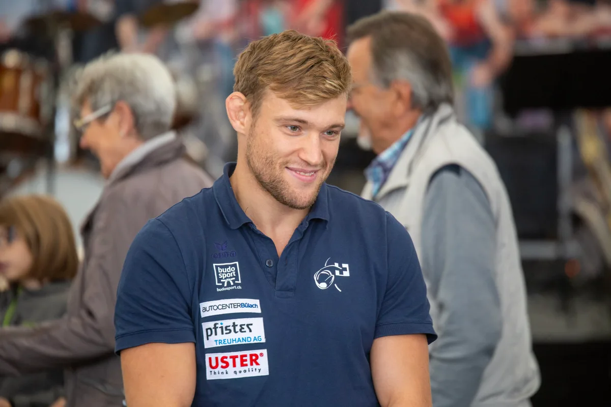 Judo-Weltmeister Nils Stump stellte sich als Überraschungsgast den Fragen aus dem Publikum. Ein junger Mann in blauem Shirt mit Sponsorenlogos.